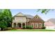Elegant brick home featuring a covered porch with columns, a balcony, manicured lawn, and lush landscaping at 1565 Briergate Dr, Duluth, GA 30097