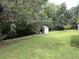 View of green backyard with storage shed nestled amongst mature trees, providing both function and natural beauty at 2529 Feathertree Ln, Lawrenceville, GA 30044
