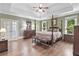 Spacious main bedroom featuring a tray ceiling, hardwood floors, and elegant four-poster bed with matching bench at 120 Forest Breeze Cv, Alpharetta, GA 30022