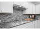 Close up on the kitchen cooktop featuring a stainless steel vent hood and mosaic tile backsplash at 127 Sanctuary Ave, Woodstock, GA 30188