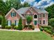 Charming brick home featuring manicured landscaping, green shutters, and a turret-style entryway, all under a blue sky at 1564 Stepstone Way, Lawrenceville, GA 30043