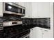 Close-up of kitchen details with stainless steel appliances, mosaic backsplash, granite counters, and white cabinetry at 13090 Magnolia Crescent Dr, Roswell, GA 30075