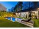 Backyard pool at dusk featuring a pool house with glass doors, lush greenery, and ambient fire features at 7165 Cordery Rd, Cumming, GA 30040