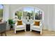 Sunroom detail showing two white armchairs with mustard pillows, a dark accent table, and an arched window with a neighborhood view at 102 Rockyford, Atlanta, GA 30317