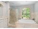 Bright bathroom featuring a soaking tub beneath a large window and a glass enclosed shower at 8643 Ellard Dr, Alpharetta, GA 30022