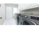 Well-lit laundry room featuring modern, front-loading washer and dryer units with white cabinets and tile flooring at 9360 Nesbit Lakes Dr, Alpharetta, GA 30022