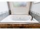A relaxing soaking tub features stone tile surround and views of the outside from the frosted window at 652 Pathview Ct, Dacula, GA 30019