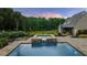 Relaxing backyard featuring a stone spa flowing into a pool, surrounded by lush landscaping and a tranquil forest backdrop at 2377 Kesgrove Way, Buford, GA 30518