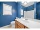 Bathroom with bold blue walls, a wood vanity, white sink and toilet, and a large mirror at 607 Little Shoals Ct, Canton, GA 30115