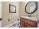 Powder room with wood cabinets, granite counters, round mirror and decorative art at 8920 Ellesmere Dr, Cumming, GA 30041