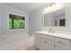 Bright bathroom with white cabinets, gold fixtures, and a large tub near a window overlooking the backyard at 2910 Leeds Garden Ln, Alpharetta, GA 30022