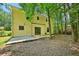 View of the backyard with a yellow home, concrete patio and mature trees at 1925 Sailcloth St, Lithonia, GA 30058