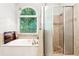 Bright bathroom featuring a soaking tub, glass-enclosed shower, and a large window with nature views at 2220 Cape Courage Way, Suwanee, GA 30024