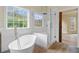This bathroom offers a modern glass enclosed shower, freestanding tub, wood-look flooring and large window at 100 Percheron Dr, Canton, GA 30114