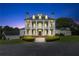 A nighttime view reveals the home's columned facade, a cupola, shutters, groomed bushes, and an adjacent garage at 2595 Ross Rd, Snellville, GA 30039