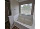 Bathroom features a tub with tile surround, wood-look flooring, and natural light from the window at 165 Heaton Place Trl, Covington, GA 30016