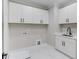 Clean laundry room features white cabinets with black hardware, a black faucet and a white marble tile floor at 37 Deer Canyon Dr, Auburn, GA 30011