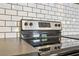 Close-up of a stainless steel oven with a black cooktop, set against a white subway tile backsplash at 355 Winding River Dr # B, Atlanta, GA 30350
