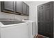 A laundry room with a full sized washer and dryer, a black door, and storage cabinets at 64 Harbour Lake Dr, Fayetteville, GA 30215