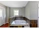 A bathtub with jets, a window, gray walls, stone tile surround, and a white door to the left at 3220 Memorial Dr, Decatur, GA 30032