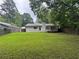 Backyard featuring a green lawn, a small deck, and a white home exterior, complemented by trees and a wooden fence at 8249 Creekline Ct, Riverdale, GA 30274