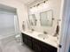 Bright bathroom with double sinks, modern lighting fixtures, dark cabinets, and a tub with tiled walls at 306 Coppergate Ct, Holly Springs, GA 30115