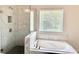 Elegant bathroom featuring a deep soaking tub, tiled shower, and a window with natural light at 306 Coppergate Ct, Holly Springs, GA 30115