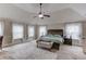 Spacious main bedroom featuring a tray ceiling, ceiling fan, carpet flooring, and large windows with sheer curtains at 206 Traditions Dr, Loganville, GA 30052