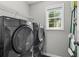Laundry room with a modern washer and dryer unit, storage shelving, and a window at 6065 Ashbury Ln, Cumming, GA 30028