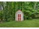 Backyard shed with red and white doors, surrounded by lush greenery and mature trees at 4200 Sterling Pointe Dr, Douglasville, GA 30135