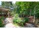Backyard entrance through wooden fence showcasing landscaping, trees, and a covered patio at 1558 Amberwood Creek Nw Dr, Kennesaw, GA 30152