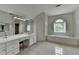 Bright bathroom featuring a large vanity, soaking tub with shuttered window and light tile floor at 12130 Helleri Holw, Alpharetta, GA 30005