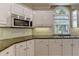 Close up of the kitchen featuring granite counters, white cabinets, stainless microwave and large window at 12130 Helleri Holw, Alpharetta, GA 30005