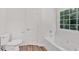 A bright bathroom with wood-look flooring includes a toilet, tub with jets and a large window at 225 Hitchcock Dr, Villa Rica, GA 30180
