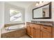 Bathroom features a tiled tub and countertop with wooden cabinets below a large mirror and a window with a view of the property at 1410 Eastland Rd Se Rd, Atlanta, GA 30316