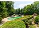 Lush backyard with pool, stone patio, mature trees, sun umbrellas, lounge chairs, and tennis court at 70 Finch Forest Trl, Atlanta, GA 30327