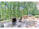 Stone patio area with built-in outdoor grill, bar, and comfortable seating surrounded by mature trees at 8240 Hurakan Creek Xing, Cumming, GA 30028
