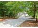 View of a long concrete driveway leading to a gray home with an attached garage, surrounded by mature trees and lush greenery at 2730 Samples Rd, Cumming, GA 30041