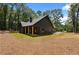 Back exterior featuring wood columns, fireplace, and beautifully manicured lawn and wooded backdrop at 1687 Harmony Rd, Temple, GA 30179
