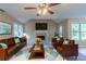 Staged living room with brick fireplace, ceiling fan, leather furniture, and large windows at 1615 Burnt Oak Way, Dacula, GA 30019