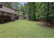 Backyard with green grass, a wooden deck, wooded area, fire pit and a fence at 9470 Hillside Dr, Roswell, GA 30076