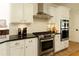 Modern kitchen with stainless steel oven, range, and hood over white cabinets and black countertops at 9975 Groomsbridge Rd, Johns Creek, GA 30022