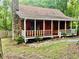 Log cabin with a stone chimney, a red door, and a white trimmed porch at 5642 Dorsett Shoals Rd, Douglasville, GA 30135