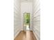 Hallway with board and batten walls and light hardwood floors leading to a glass paneled door at 10904 Serenbe Ln, Chattahoochee Hills, GA 30268