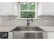 Close-up of stainless steel farmhouse sink with granite countertop and tiled backsplash at 2565 Aaron Ct, Loganville, GA 30052
