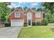 Charming brick home with a well-manicured lawn and a two-car garage, framed by lush trees on a sunny day at 5015 Riverthur Pl, Peachtree Corners, GA 30096