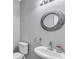 Compact half bathroom featuring a modern round mirror, a pedestal sink, and a toilet, creating a functional space at 217 Odyssey Turn, Conyers, GA 30012