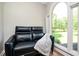 Cozy sitting area with black leather couch, blanket, and arched window overlooking green landscape at 13789 Woolsey Rd, Hampton, GA 30228