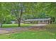 Traditional brick ranch-style home with covered porch, long driveway, and mature trees in a lush green yard at 1724 Rhonda Ln, Stone Mountain, GA 30087