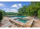Backyard pool and spa surrounded by a stone patio, greenery, and mature trees under a blue sky at 4935 Stablegate Ct, Cumming, GA 30028